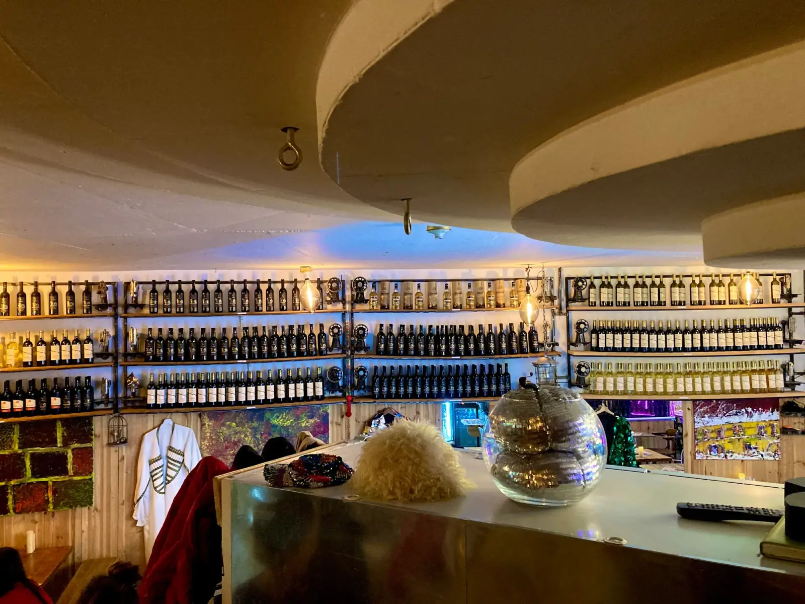 Bar vor einer Wand voller Weinflaschen, daneben eine georgische Tschocha und Papacha-Mützen